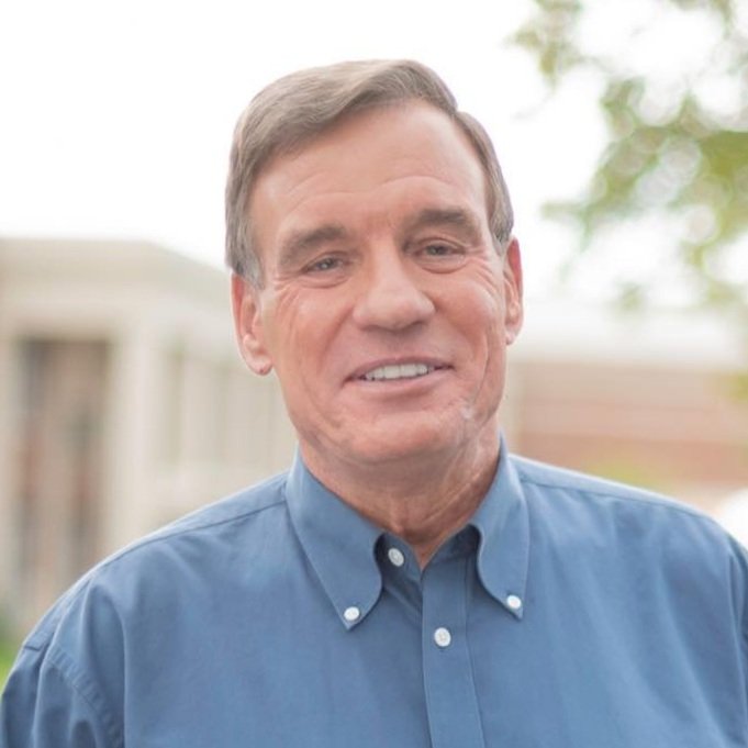 A smiling man in a blue button-up shirt outdoors.
